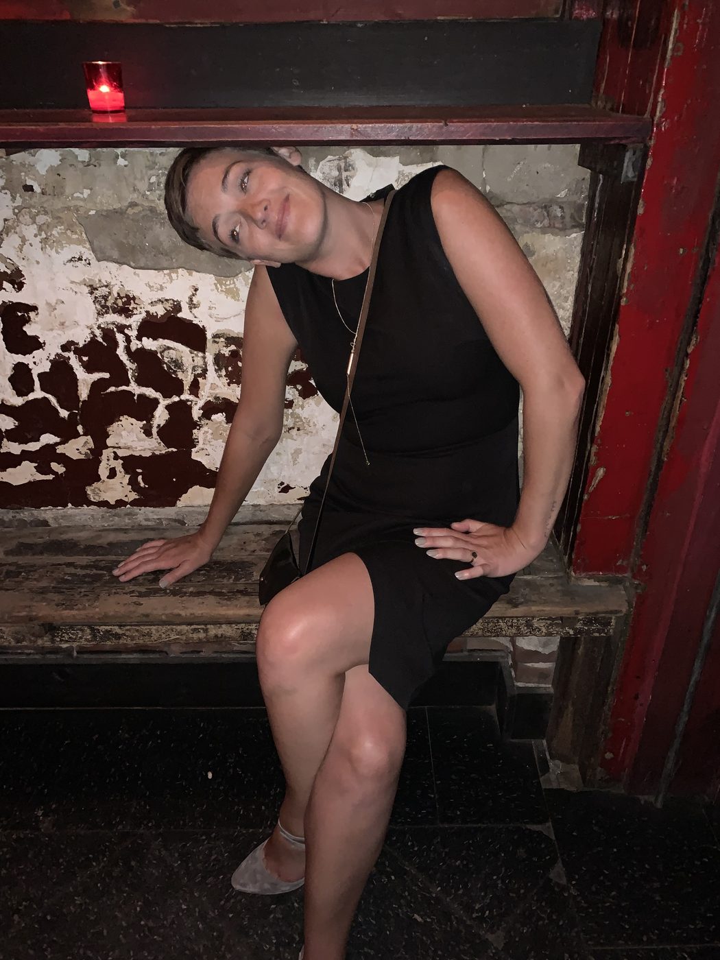 Cassie in a black dress, leaning against a bar